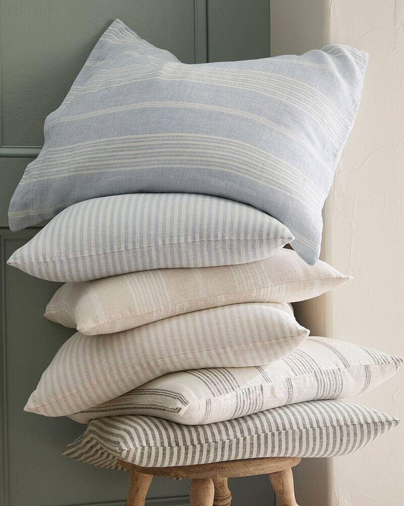 A stack of pillows in striped relaxed linen pillowcases. Browse all sheets.